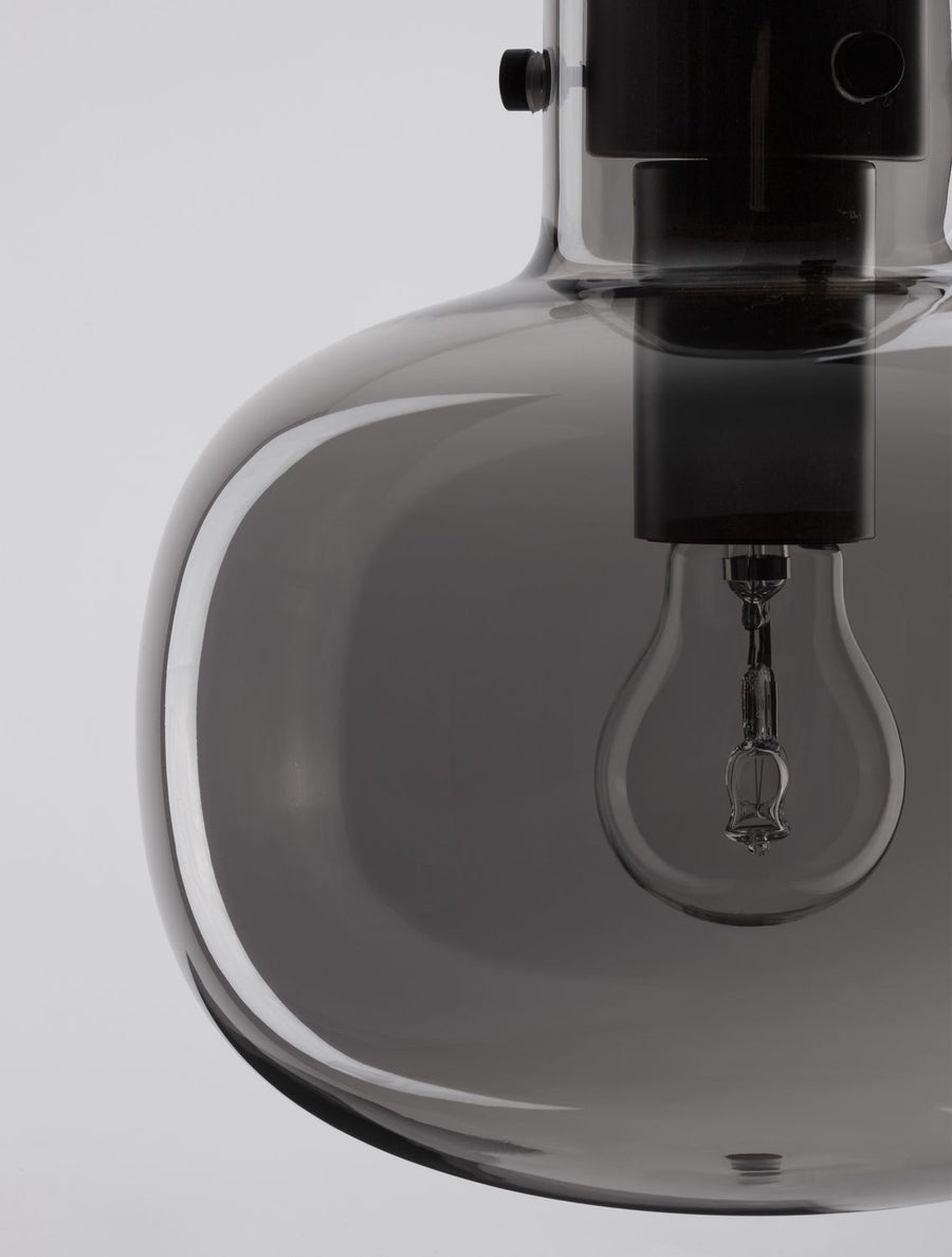 Gros plan sur l'abat-jour bombé en verre fumé et l'ampoule visible