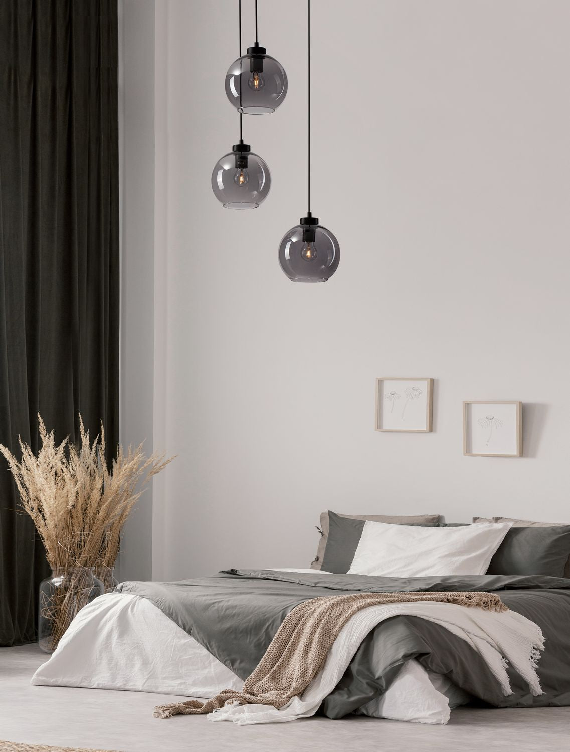 Mise en ambiance : suspension à trois globes en verre fumé au-dessus d'un lit gris et blanc.