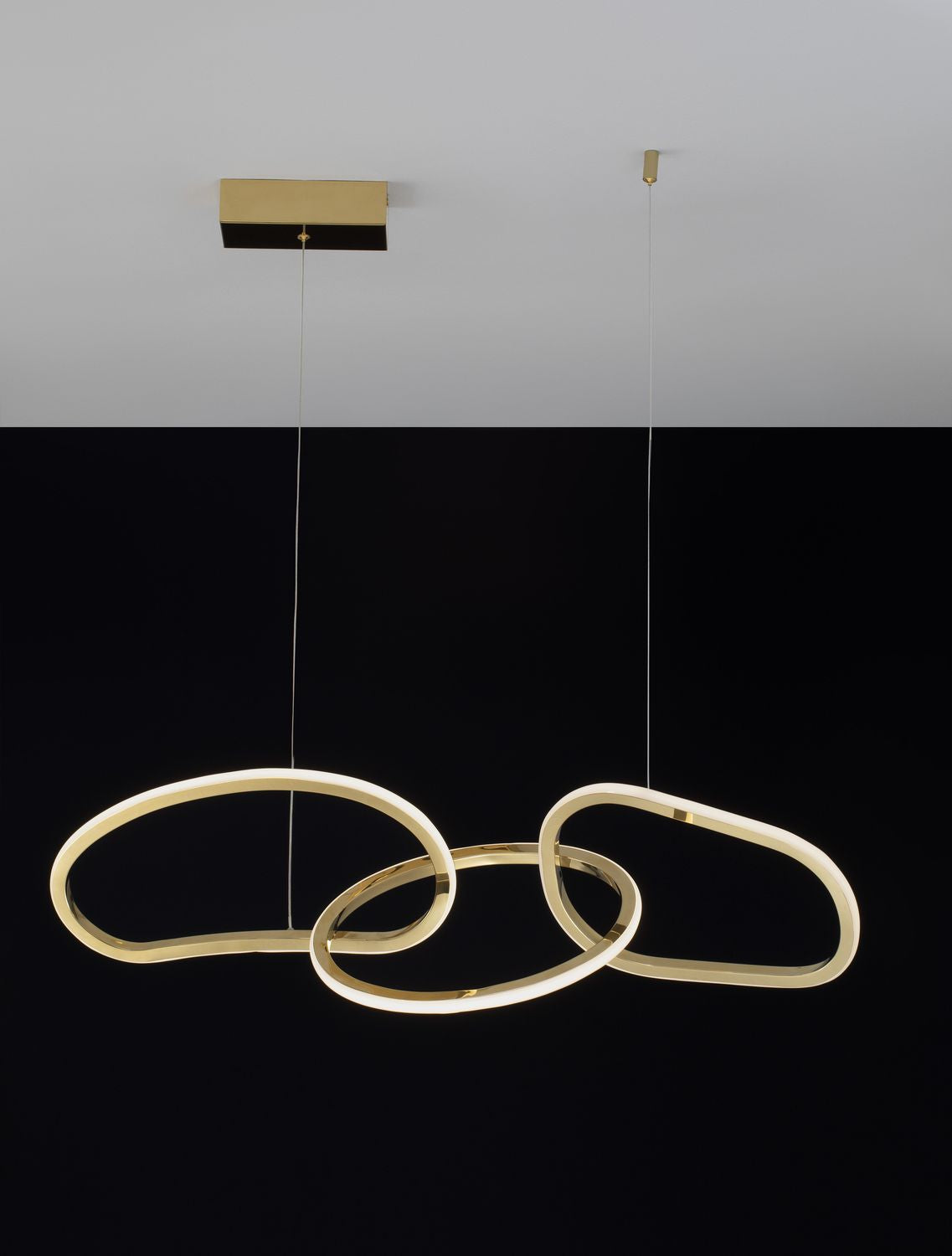 Luminaire allumé sur fond noir, anneaux dorés soulignant la lumière blanche