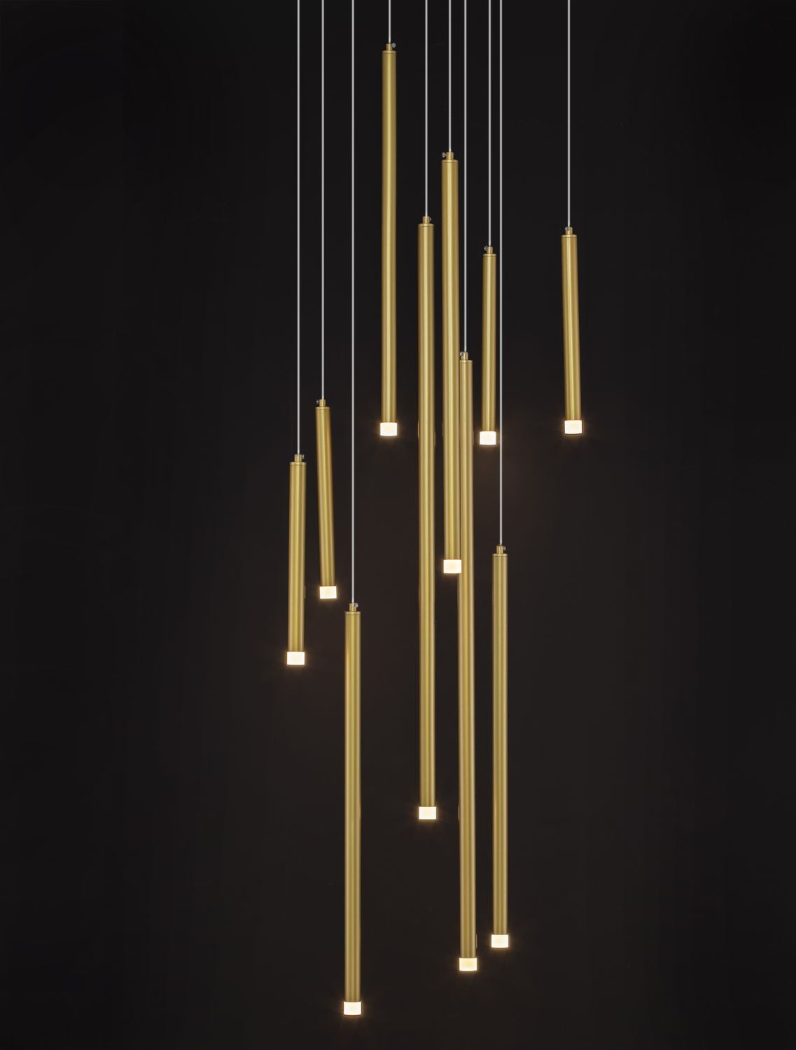 Suspension dorée allumée sur fond noir, points lumineux aux extrémités des tubes.