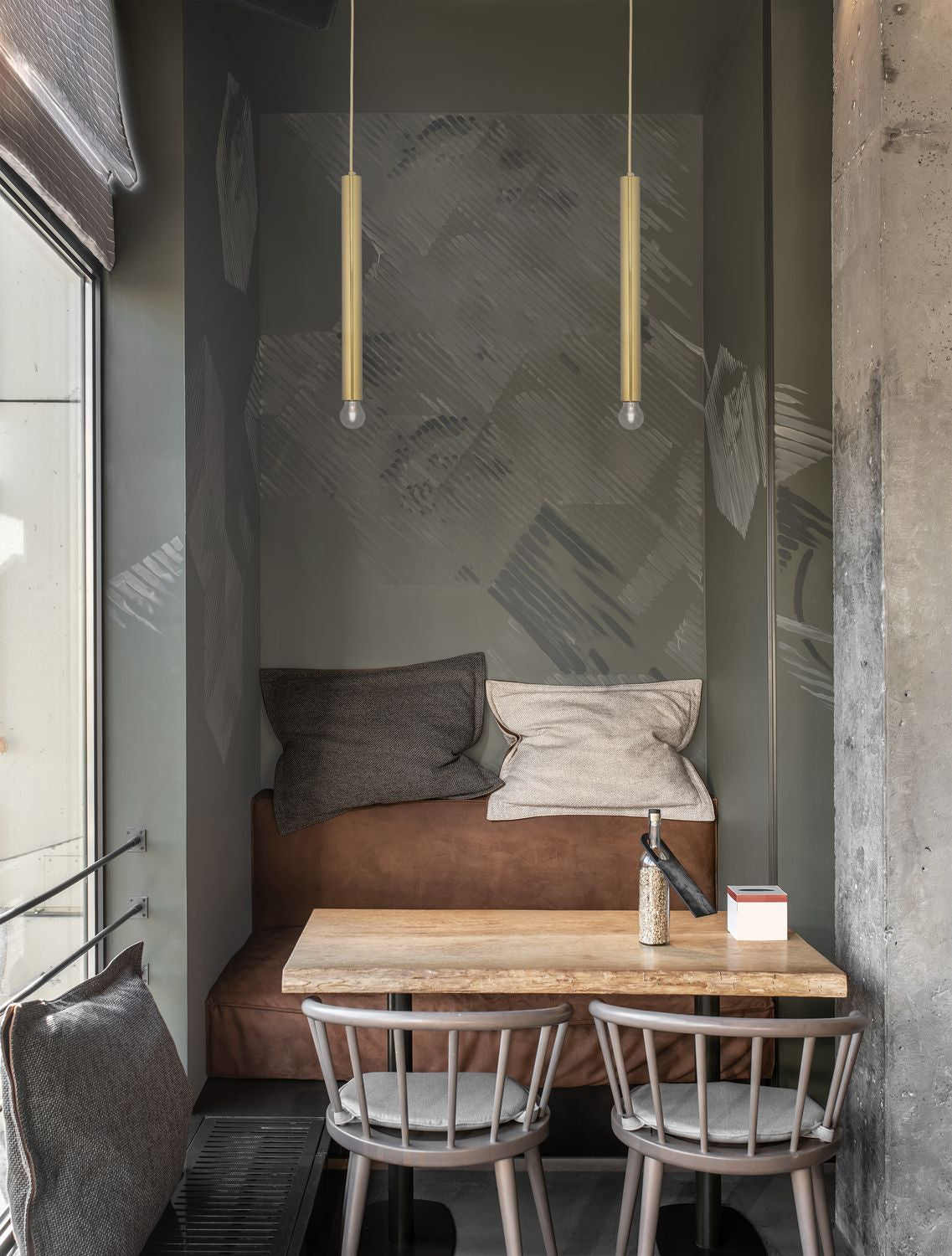 Mise en ambiance : deux suspensions dorées éclairant une table de restaurant au mur gris