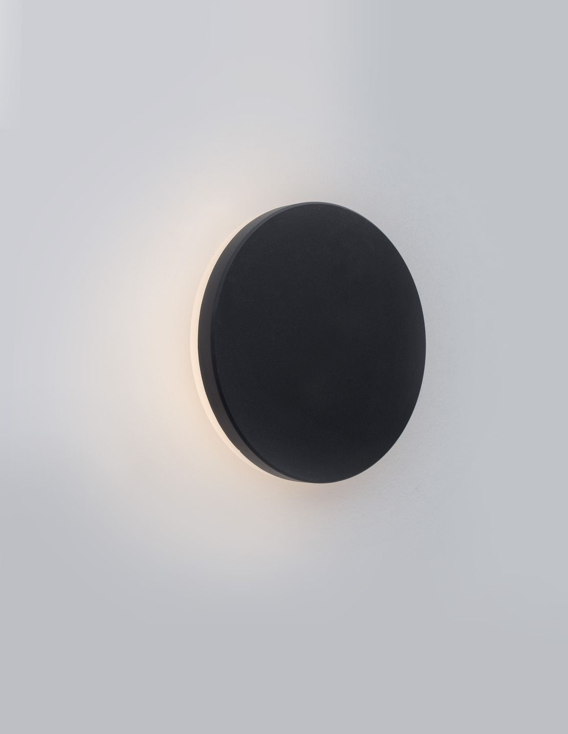 Applique murale ronde noire allumée sur un mur blanc, halo lumineux diffus