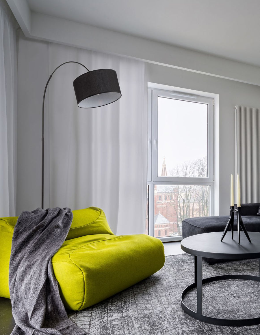 Lampadaire noir en situation dans un salon, canapé vert et grande fenêtre