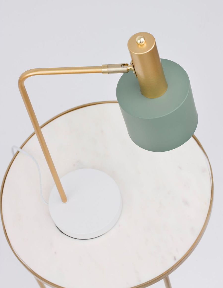 Lampe à poser dorée et verte posée sur une table ronde blanche, vue plongeante.