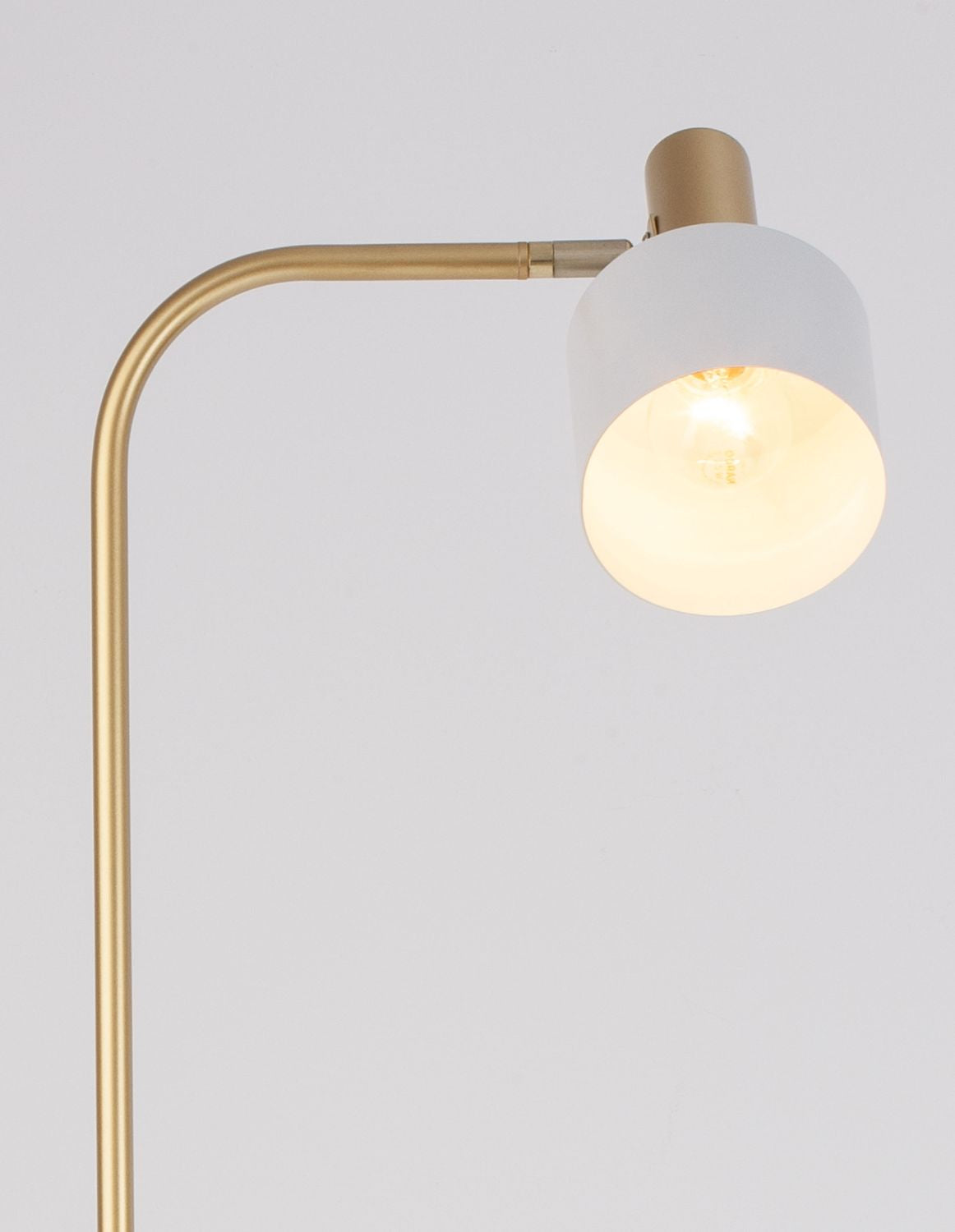 Détail du diffuseur blanc cylindrique et de l'armature dorée recourbée, ampoule allumée.