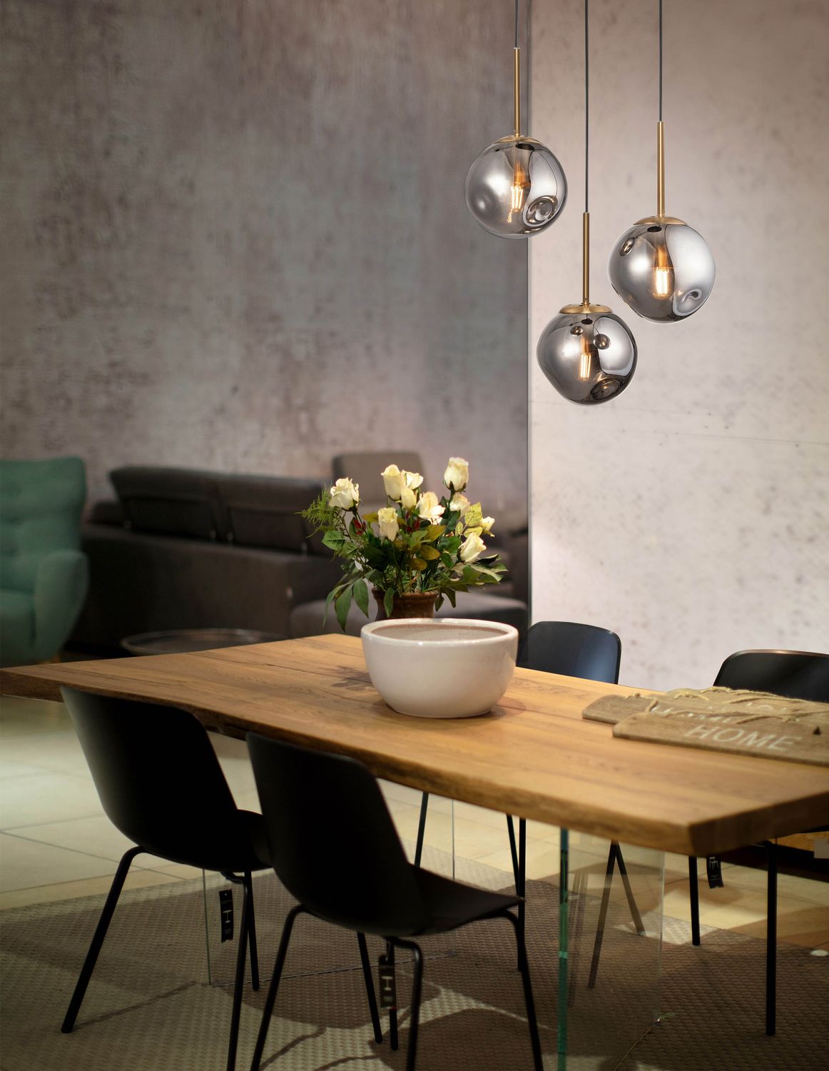 Suspension trois globes en verre fumé doré au-dessus d'une table en bois avec chaises noires