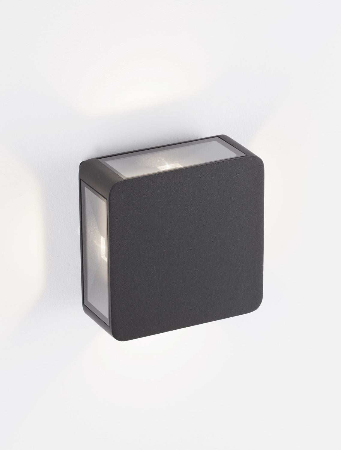 Vue trois quarts de l'applique murale anthracite carrée fixée sur un mur blanc