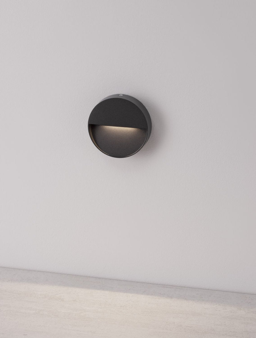 Applique murale ronde éclairée, diffusant une lumière rasante sur un mur blanc.
