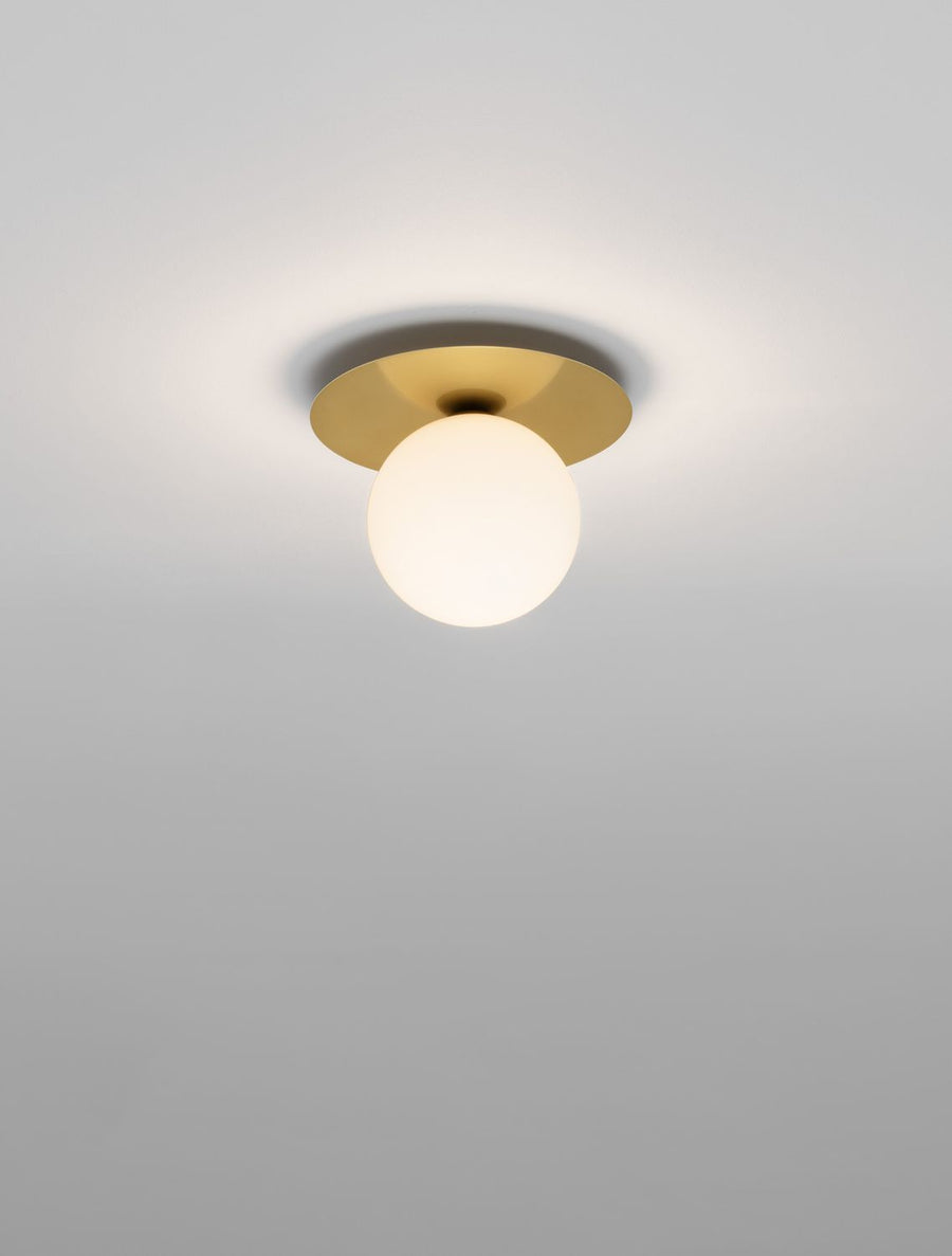 Plafonnier doré allumé fixé au plafond blanc, globe de verre opalin diffusant une lumière douce