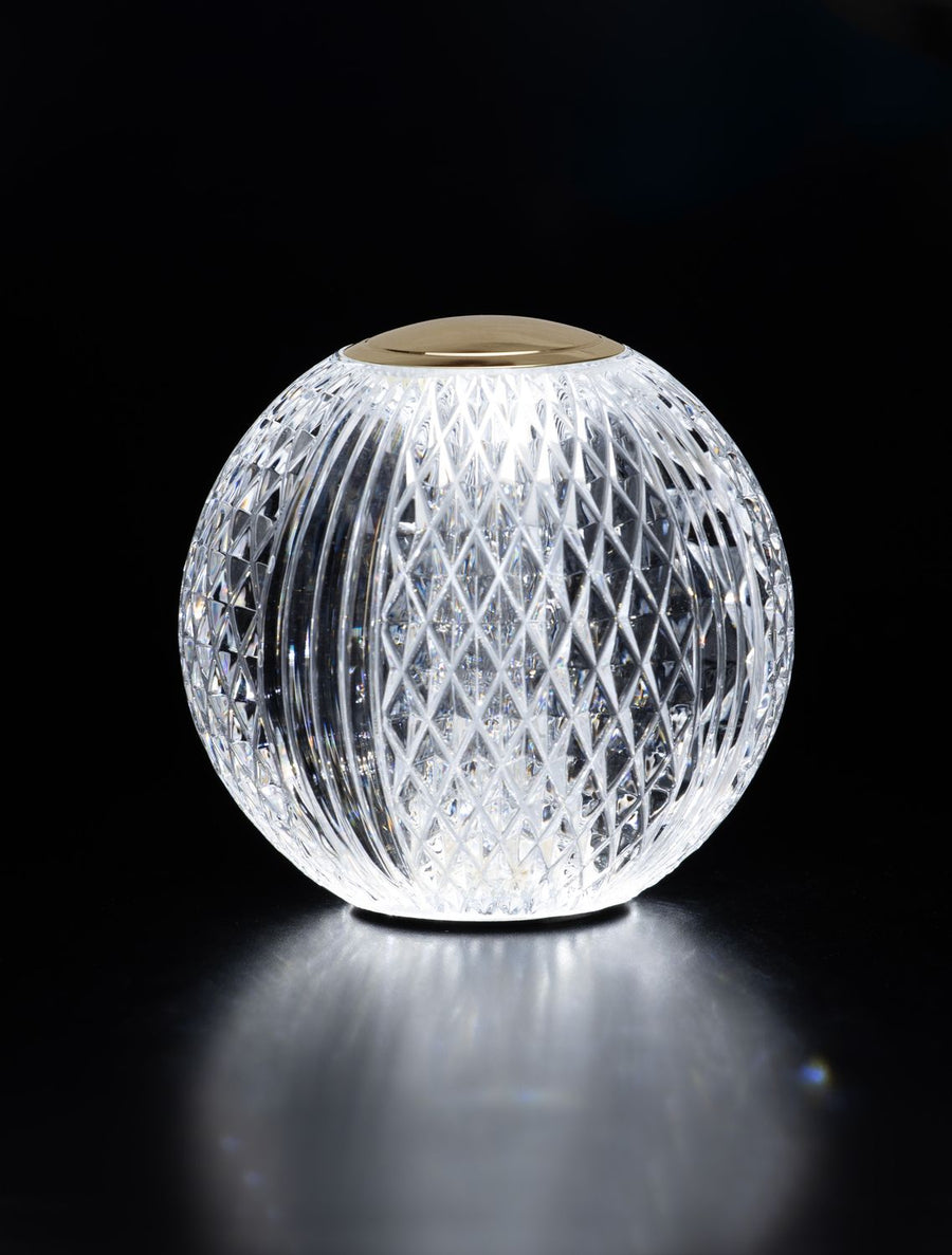 Photo sur fond noir, lampe allumée en contre-jour, reflets dorés et transparence du verre.