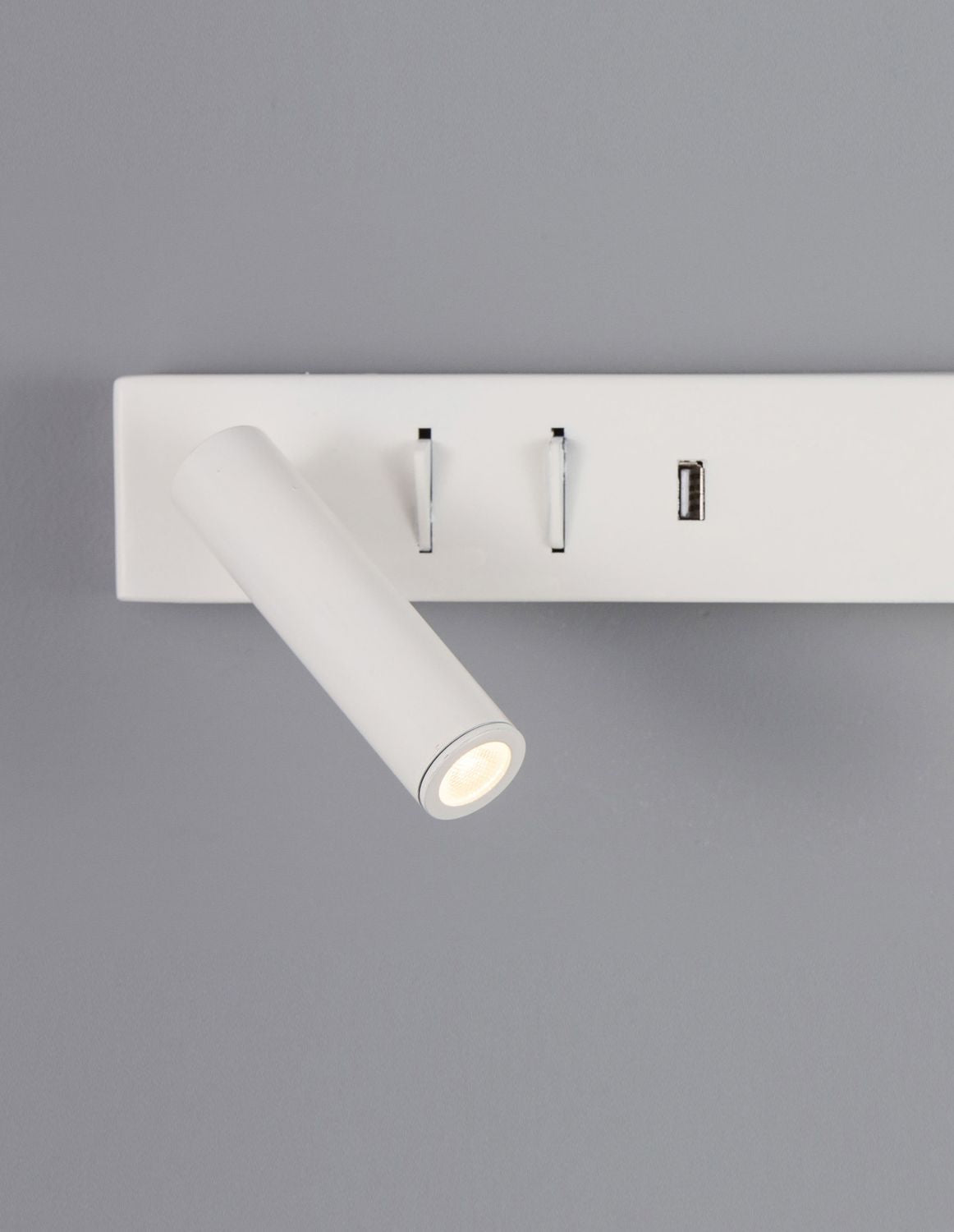 Détail rapproché du spot orientable et des interrupteurs chromés sur fond gris
