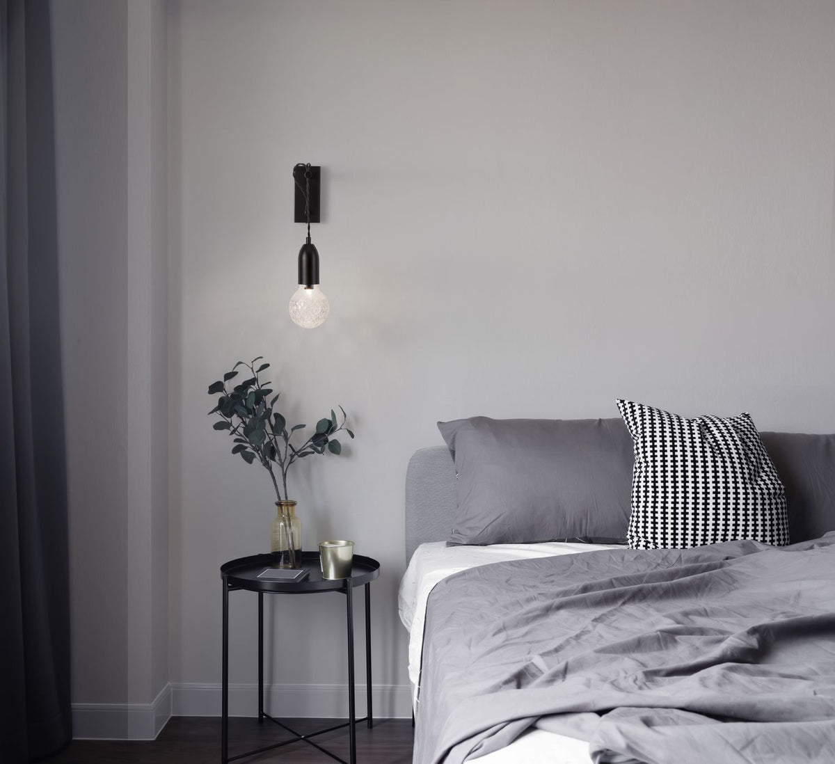 Mise en ambiance d'une chambre, applique murale noire allumée au-dessus d'une table de nuit.