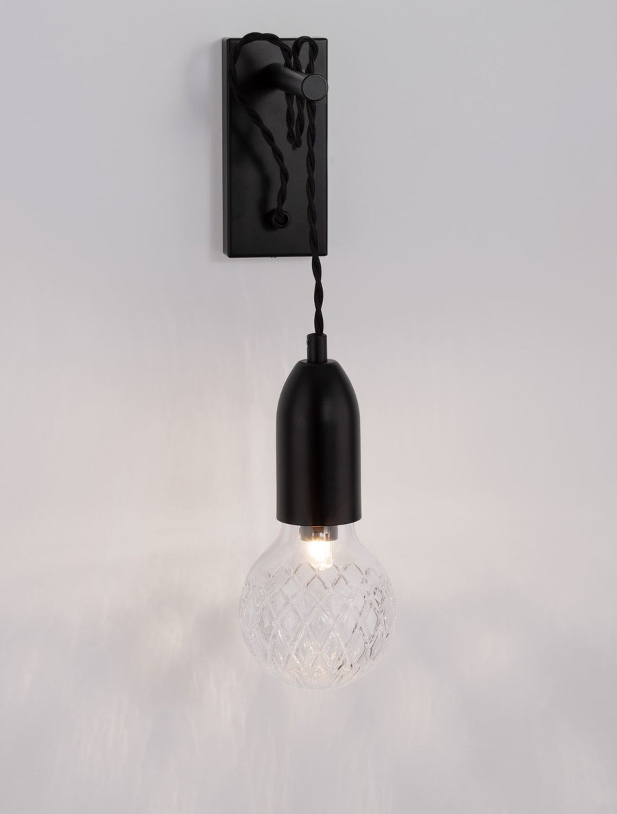 Gros plan sur la douille cylindrique noire et l'ampoule en verre texturé.