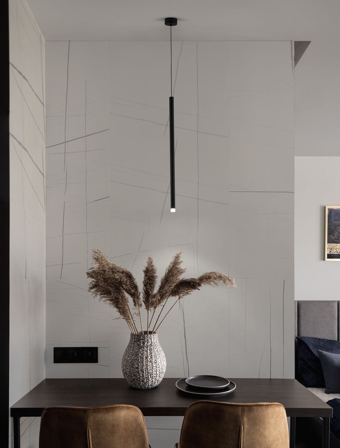 Photo d'ambiance : suspension noire allumée au-dessus d'une table avec vase de fleurs séchées.
