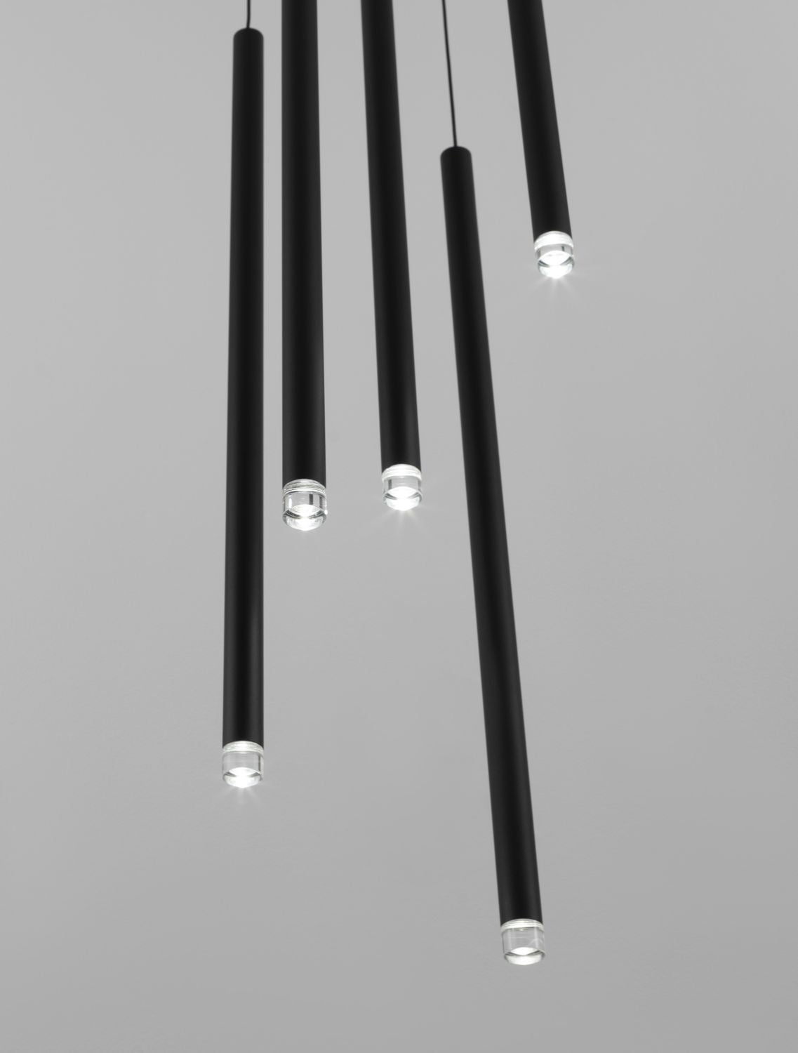 Gros plan sur cinq tubes noirs suspendus, diffuseurs transparents allumés sur fond gris.