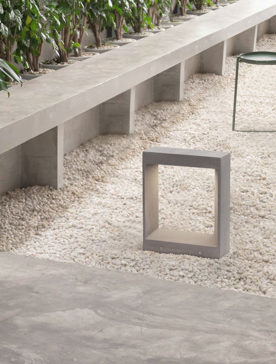 Borne extérieure grise installée sur lit de gravier blanc dans un jardin contemporain.