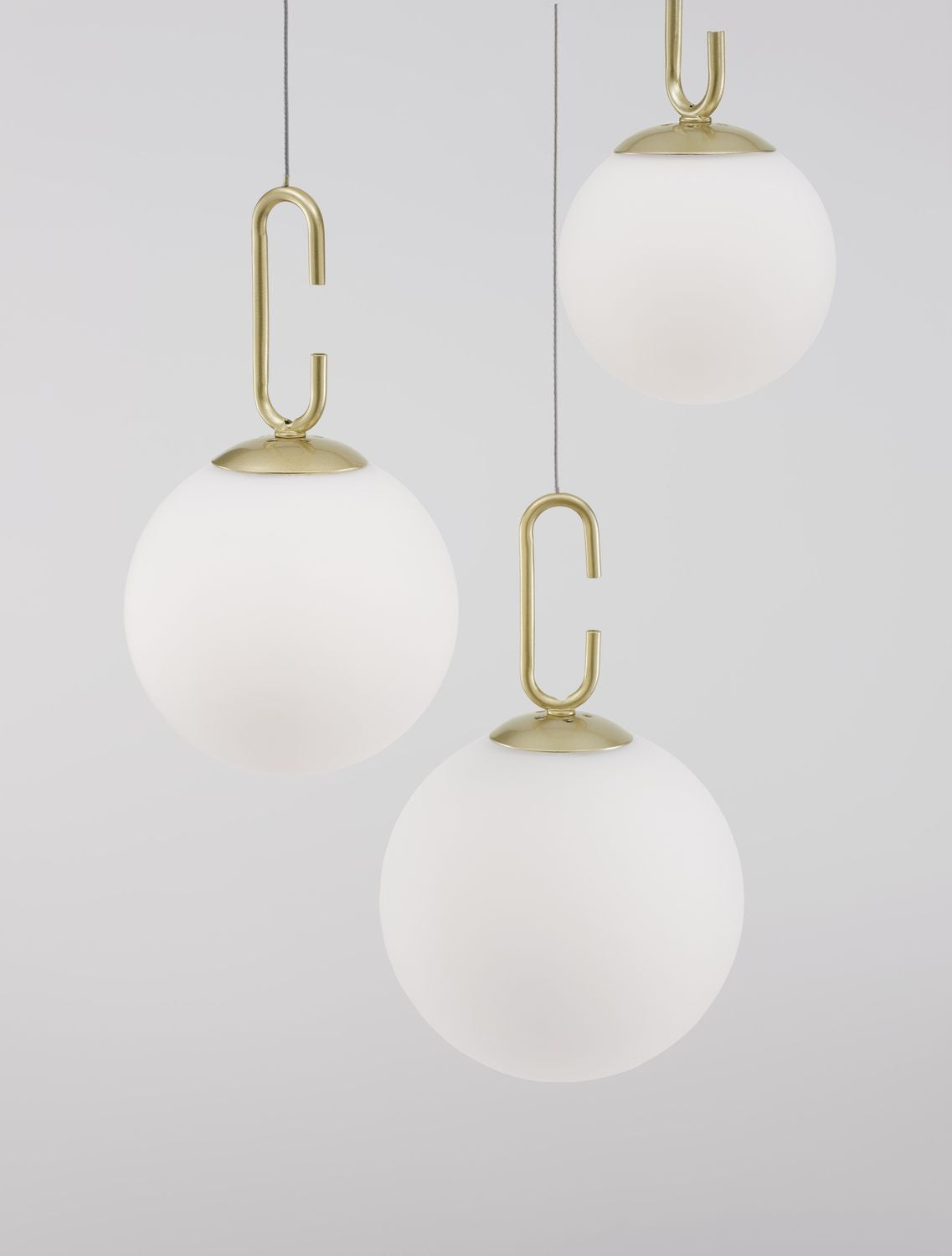 Gros plan sur trois globes de verre opalin et leurs crochets dorés en métal.