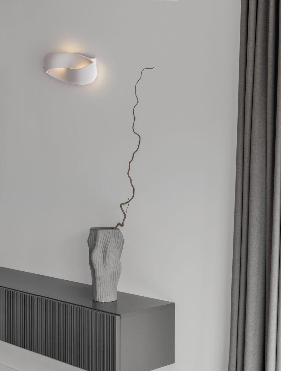 Applique murale blanche allumée, fixée sur un mur gris dans un intérieur épuré