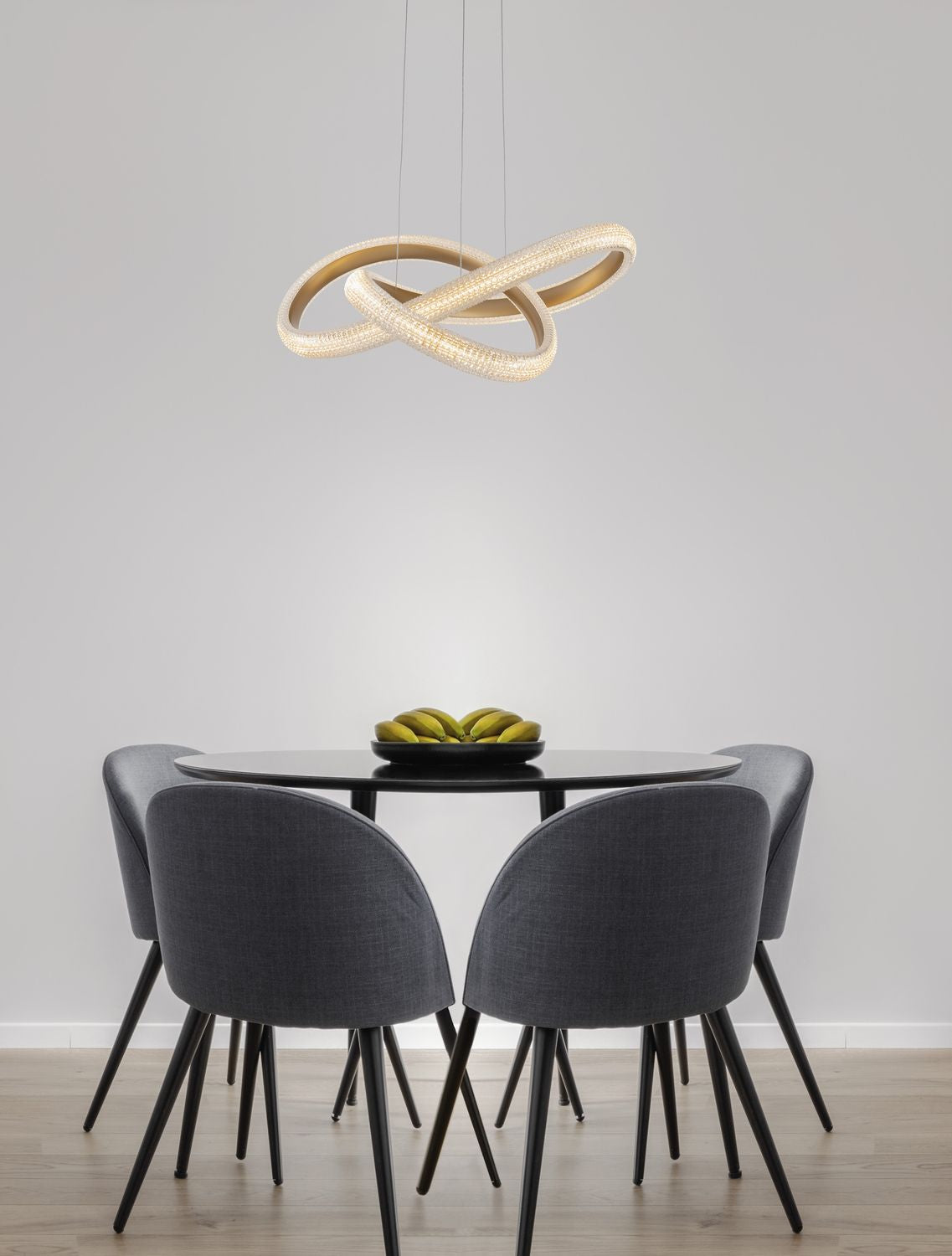 Suspension allumée au-dessus d'une table à manger entourée de quatre chaises grises.
