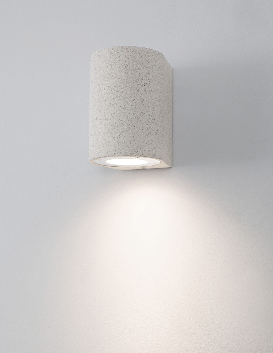 Applique murale blanche allumée sur mur clair, halo de lumière diffuse vers le bas.