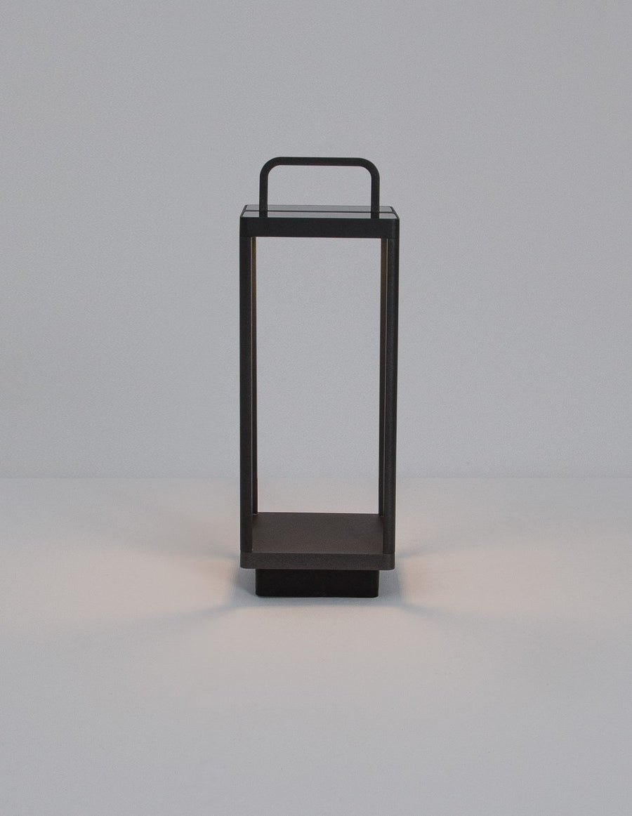 Vue de face du luminaire anthracite, structure rectangulaire ajourée, poignée et socle apparents.