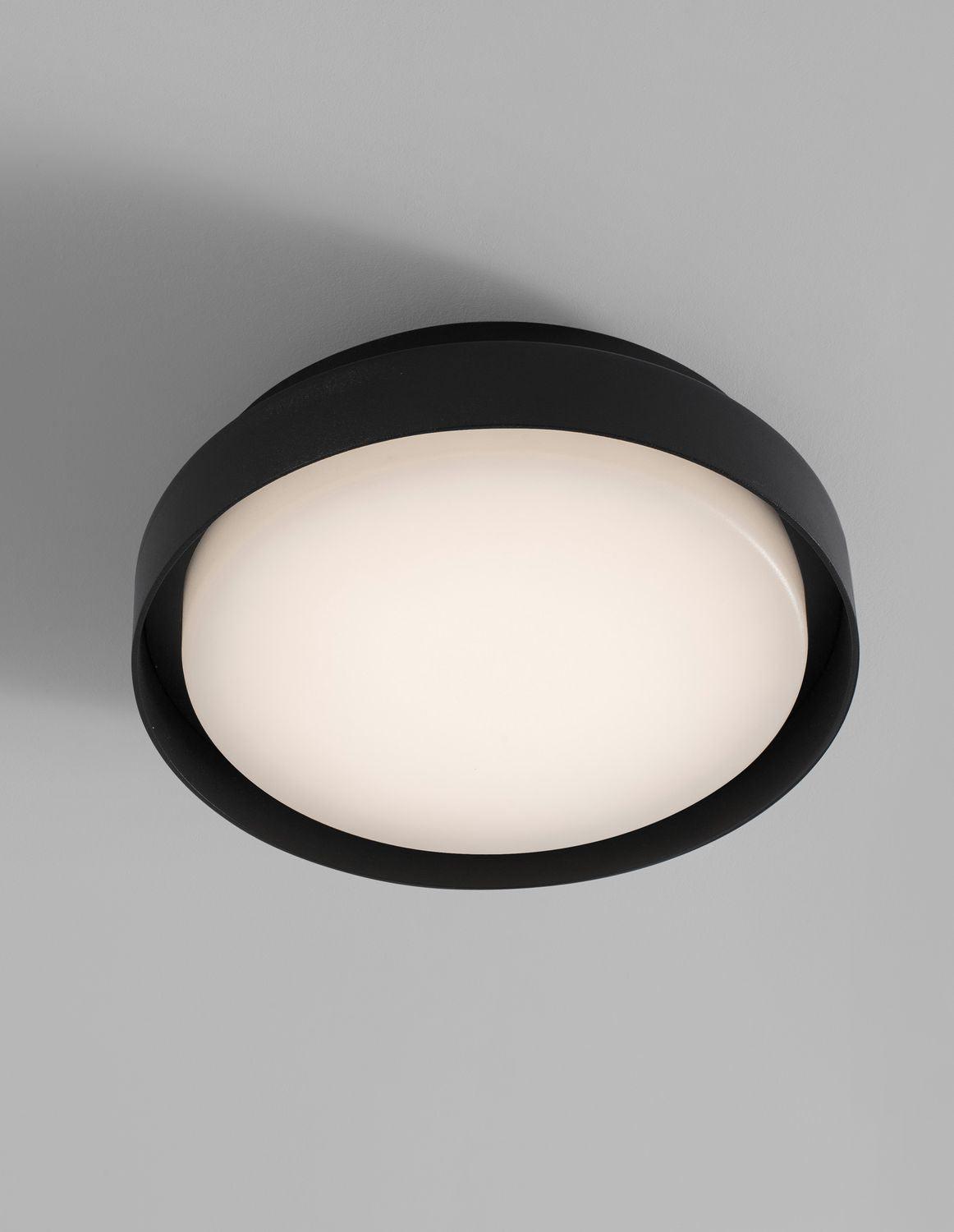 Gros plan du luminaire allumé, cerclage noir et diffuseur blanc bombé