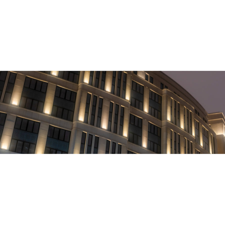 Façade d'immeuble éclairée de nuit par des luminaires linéaires verticaux.