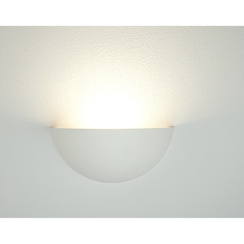 Gros plan sur l'applique murale demi-sphère allumée, halo lumineux doux sur le mur.