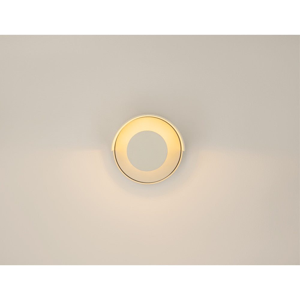 Applique murale ronde allumée fixée sur un mur beige, diffusant une lumière chaude.