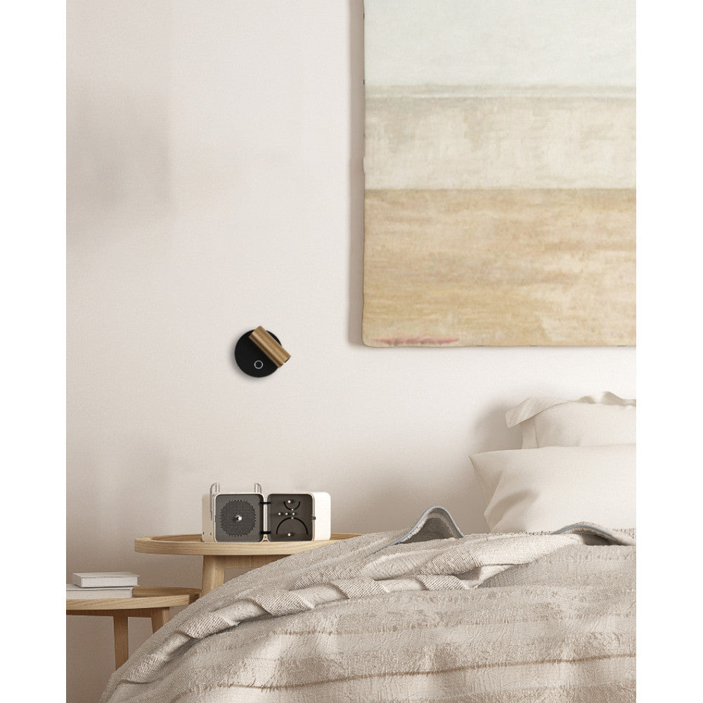 Mise en ambiance chambre, applique murale noire et or allumée au-dessus d'une table de nuit
