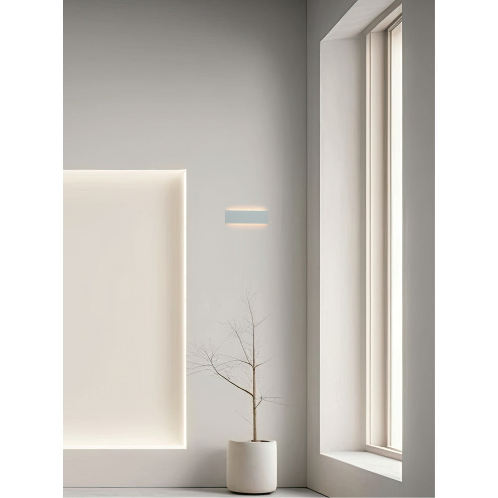 Mise en ambiance minimaliste : applique murale rectangulaire éclairant un mur gris près d'une fenêtre.