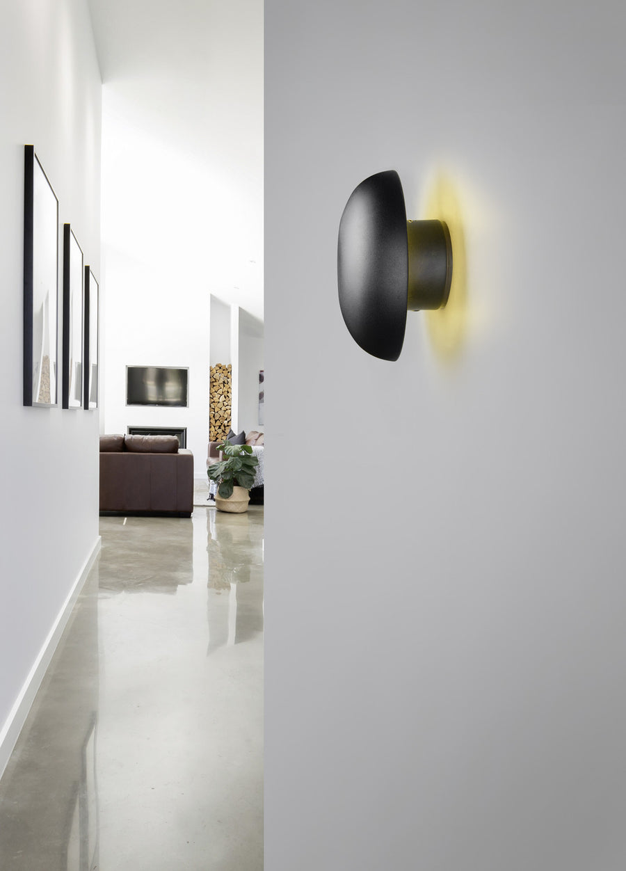 Applique murale noire allumée sur mur blanc, halo de lumière chaude dans un intérieur