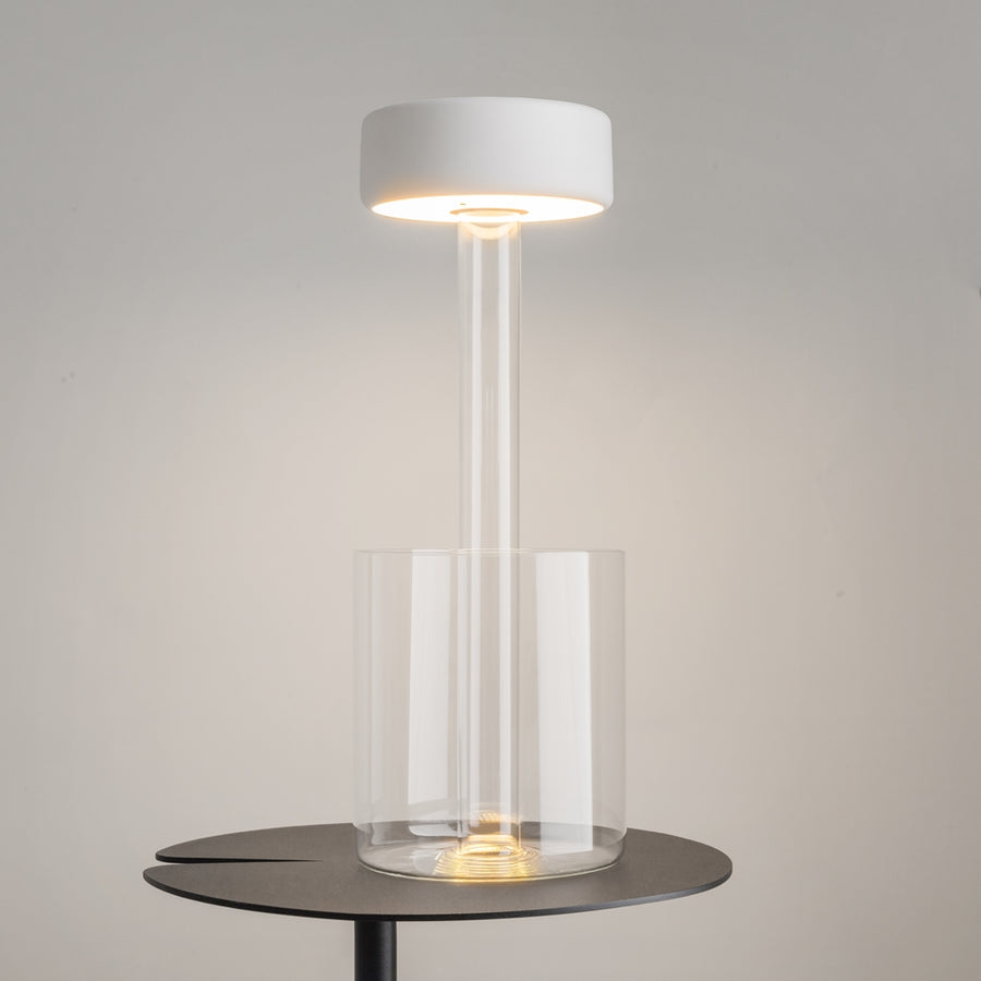 Lampe allumée posée sur une table ronde sombre, halo chaud diffus