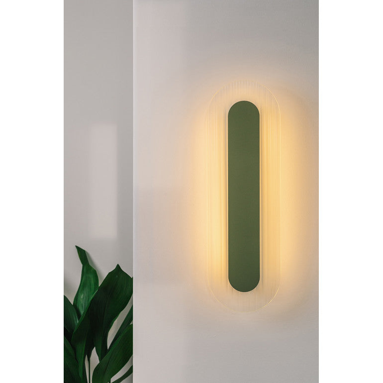Mise en ambiance sur mur blanc, halo lumineux chaud diffusé autour de l'applique verte