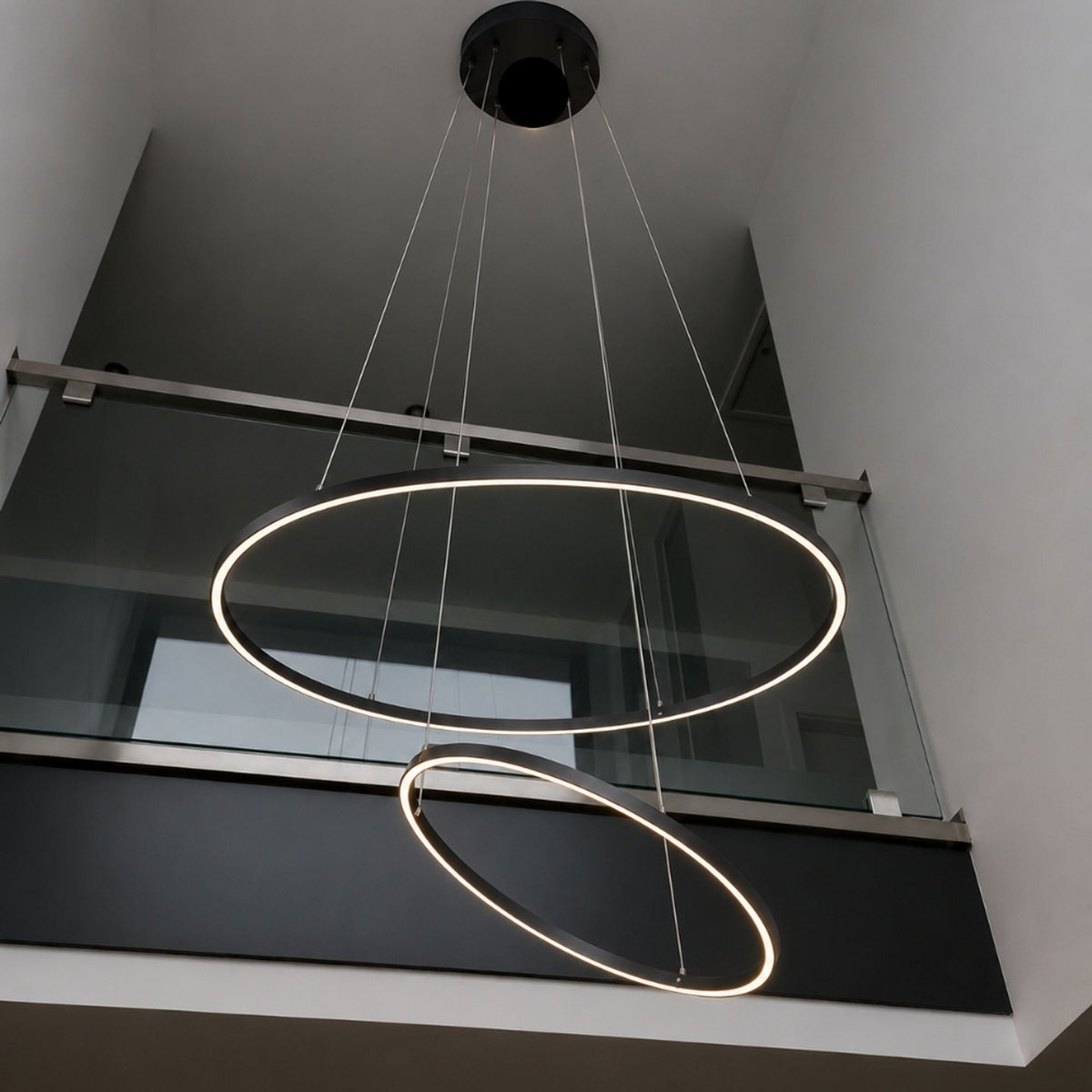 Deux anneaux LED noirs suspendus, vus en contre-plongée dans une cage d'escalier vitrée