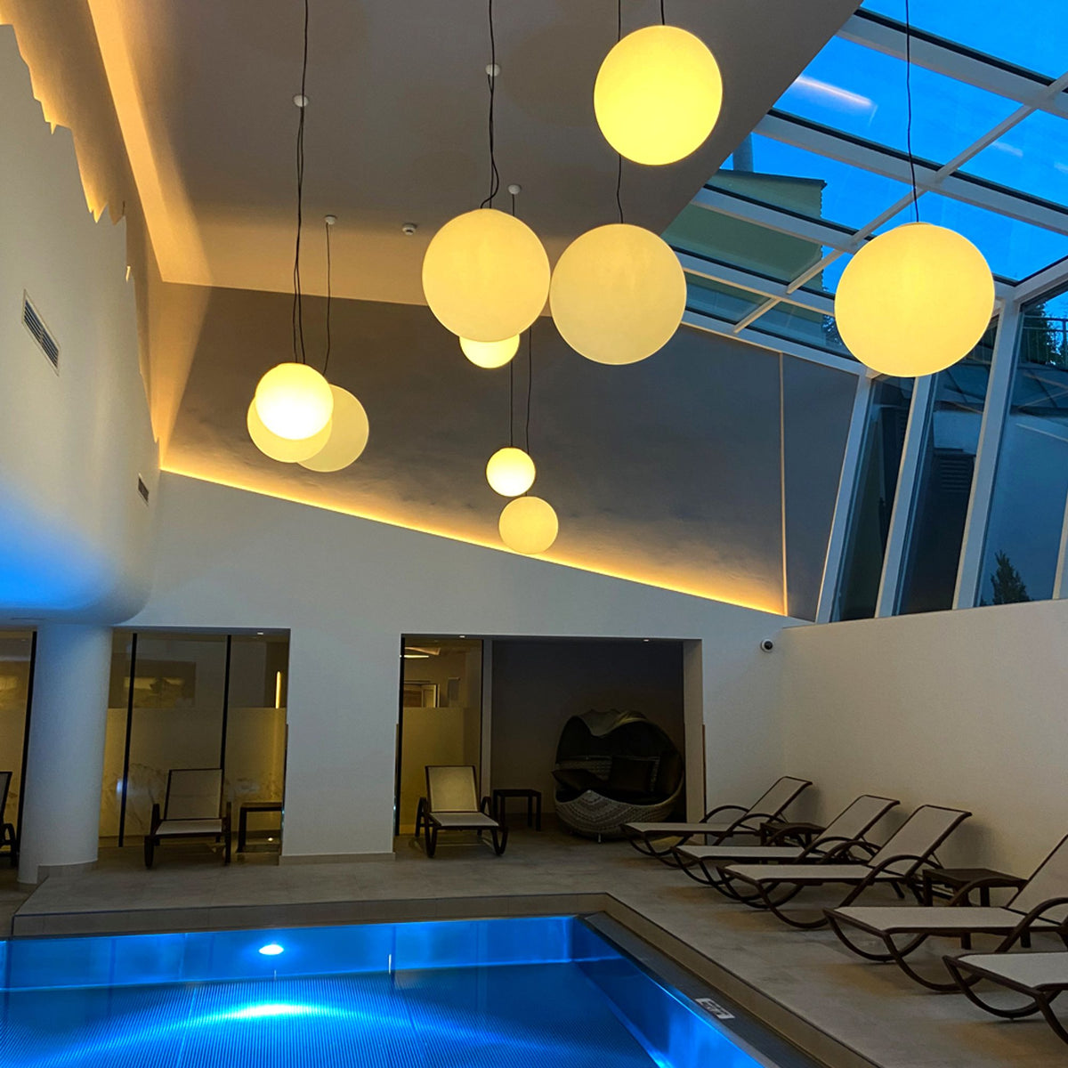 Globes suspendus au-dessus d'un bassin intérieur sous verrière, piscine et transats