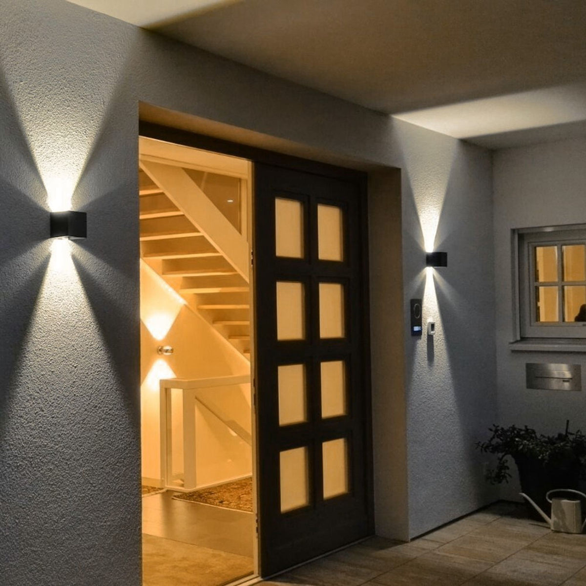 Entrée extérieure avec deux appliques cubes encadrant une porte ouverte