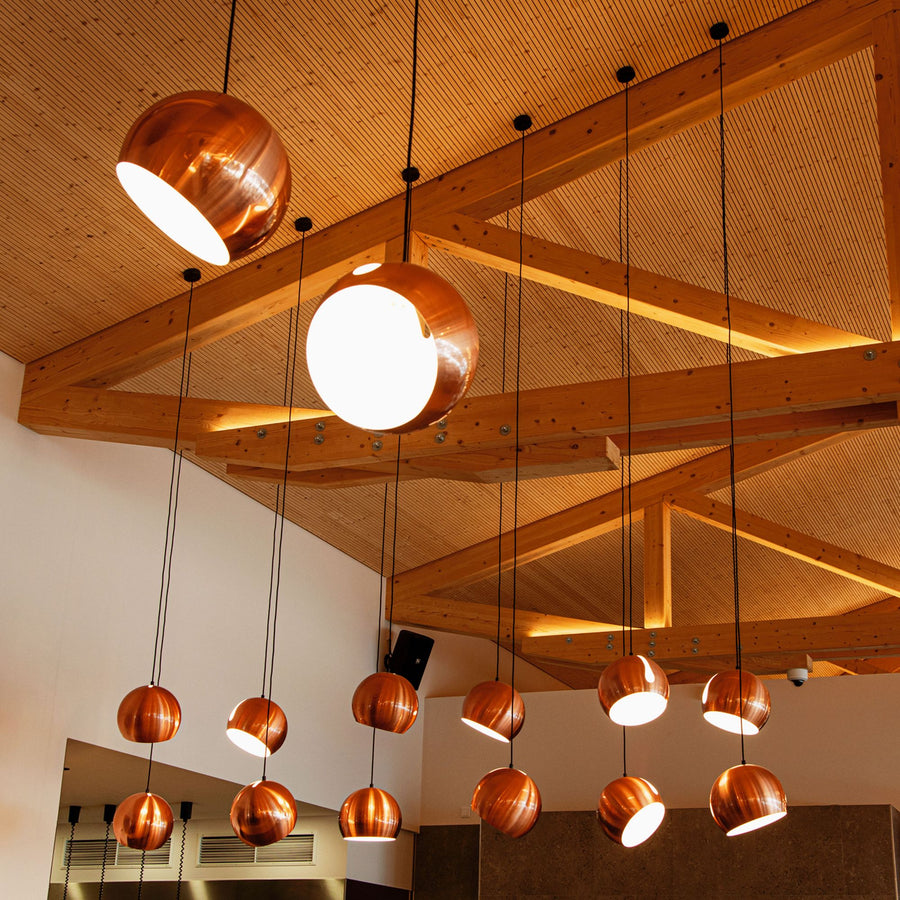 Plafond en bois et nombreuses suspensions cuivrées de hauteurs variées dans un grand volume