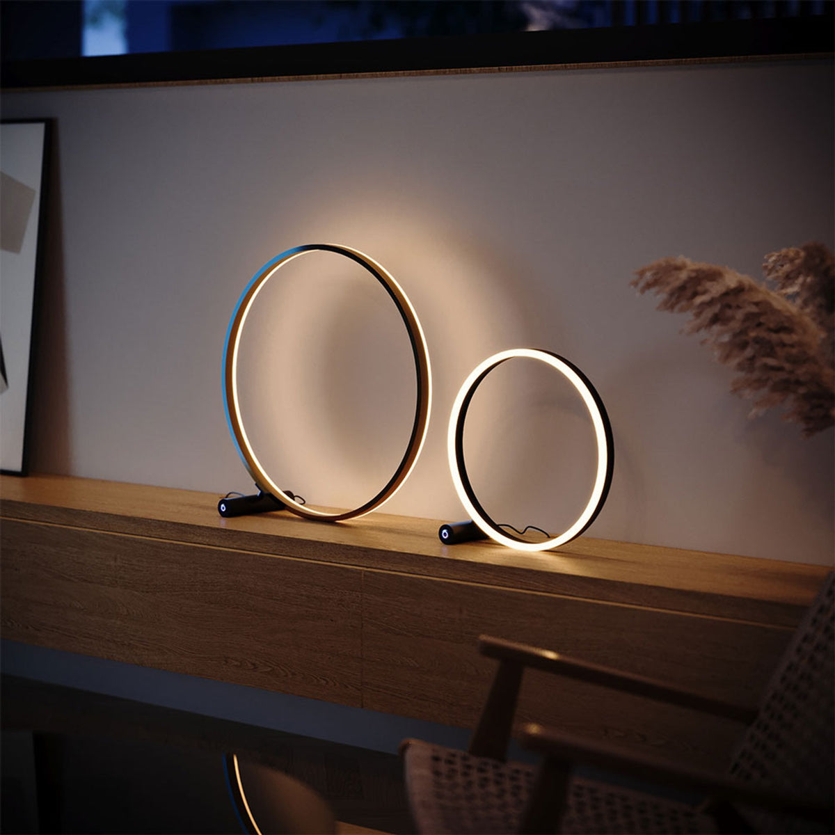 Deux lampes annulaires LED allumées posées sur un meuble en bois, lumière chaude directe et indirecte