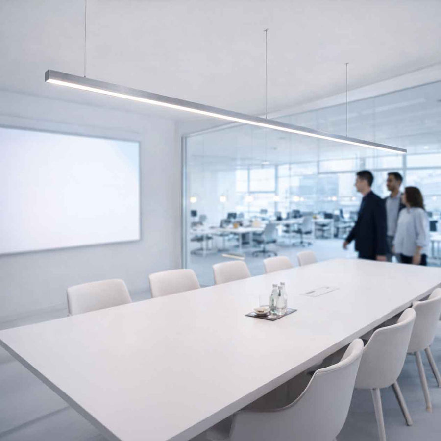 Suspension linéaire blanche allumée au-dessus d'une longue table de réunion en bureau vitré