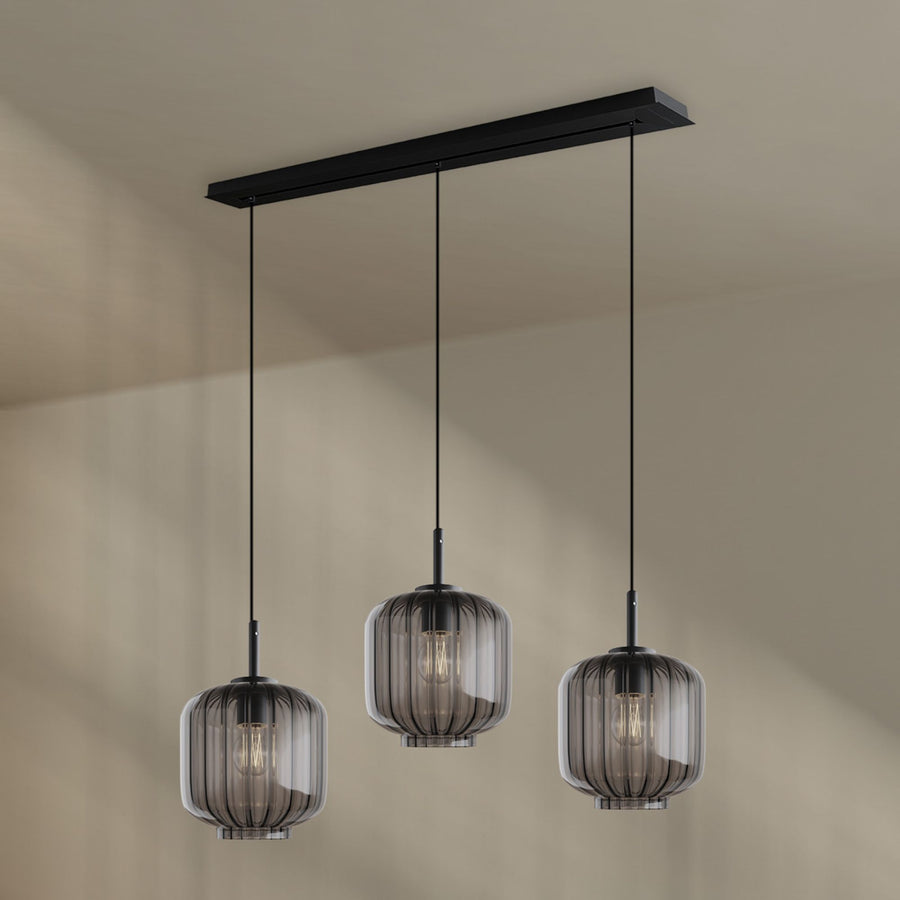 Luminaire à trois verres fumés translucides suspendus devant un mur beige