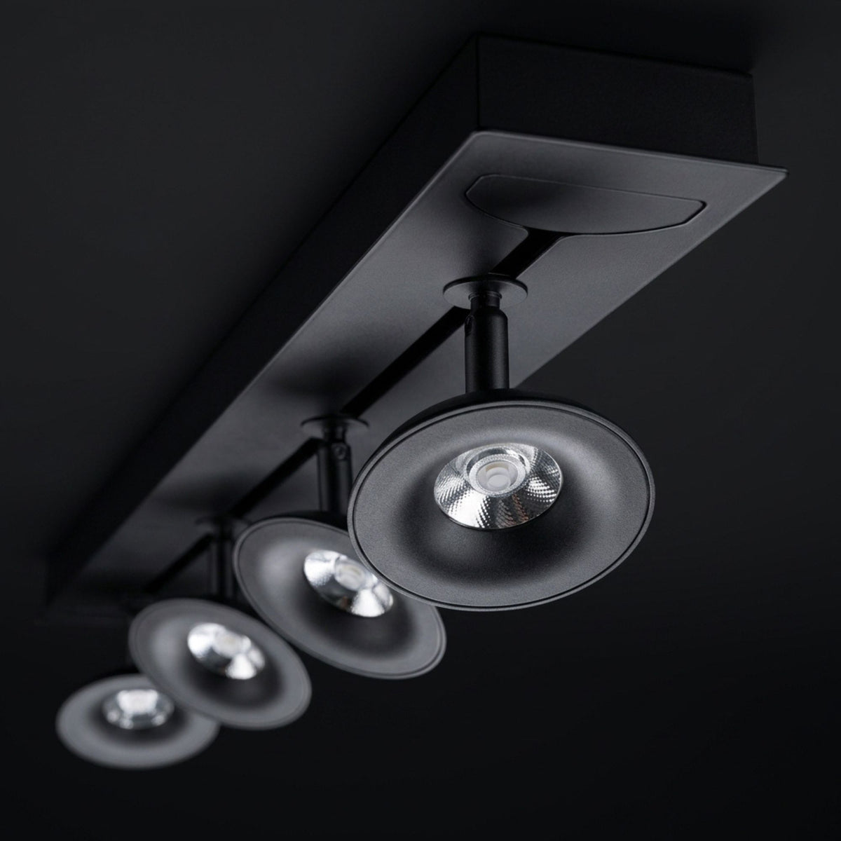 Rail noir avec quatre spots orientables alignés, vus de dessous sur fond sombre