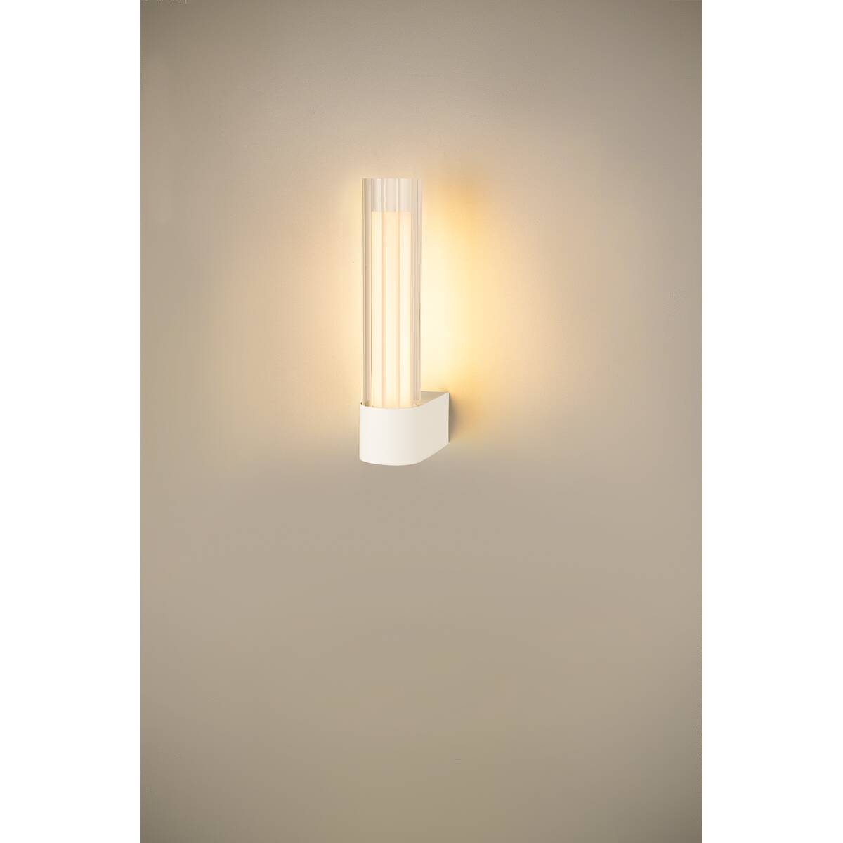 Applique allumée fixée au mur, halo chaud projeté sur la paroi beige.