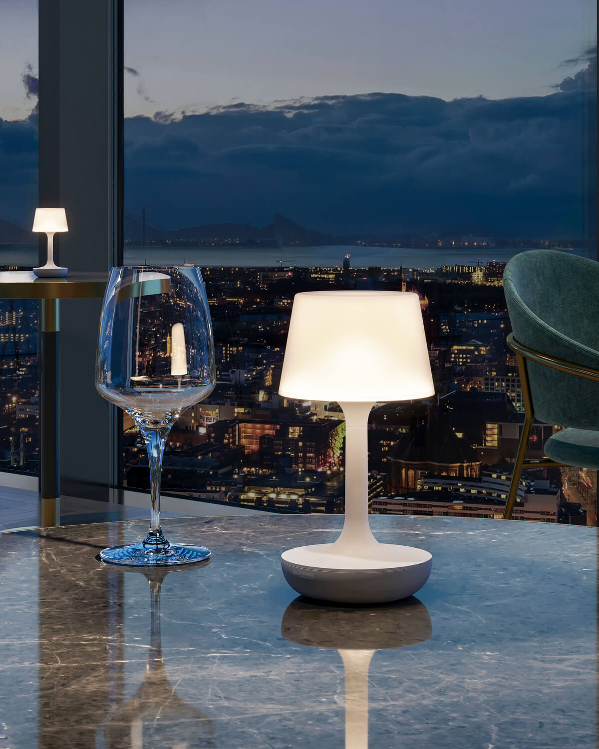 Lampe allumée posée sur une table en marbre devant une vue nocturne de ville.