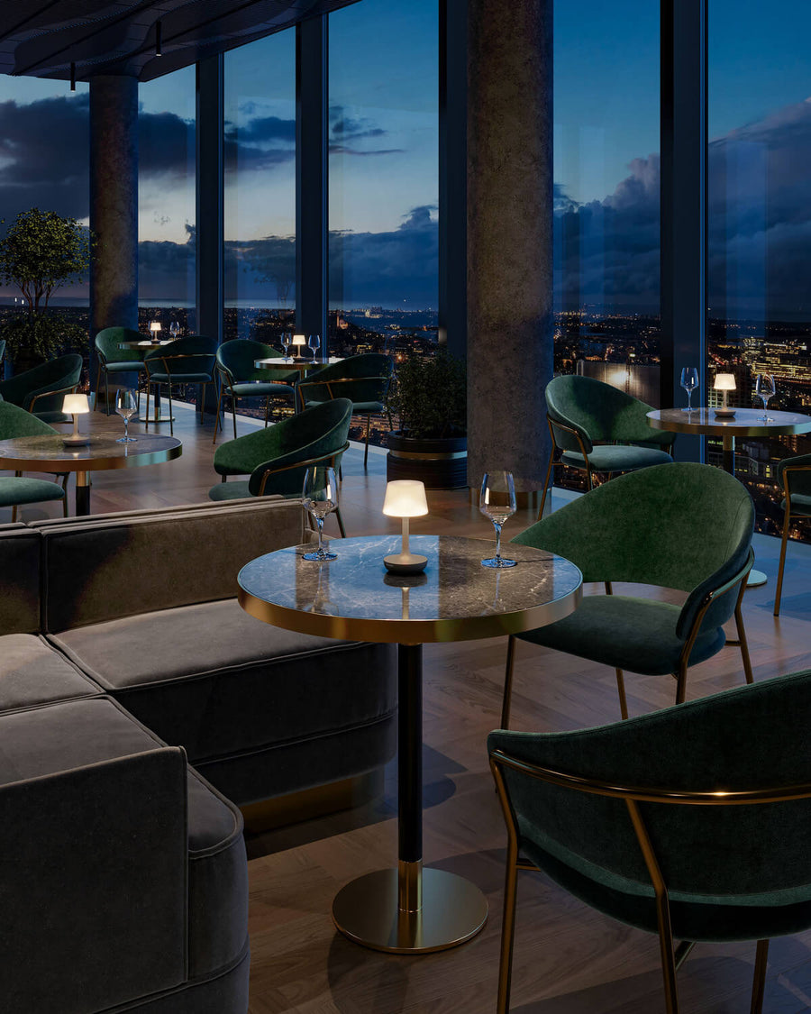 Plusieurs lampes beiges éclairent des tables de bar avec fauteuils verts et vue nocturne.