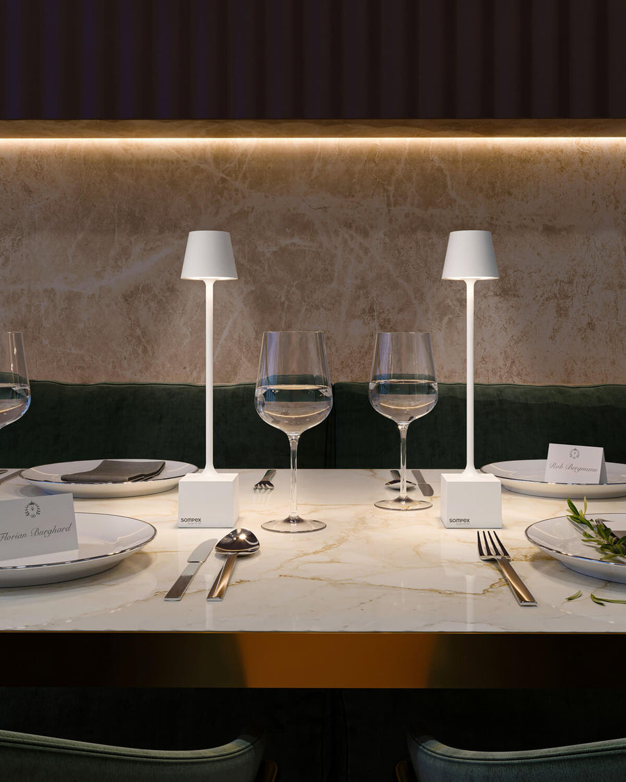 Détail de table dressée avec deux lampes blanches, verres et cartons de menu.
