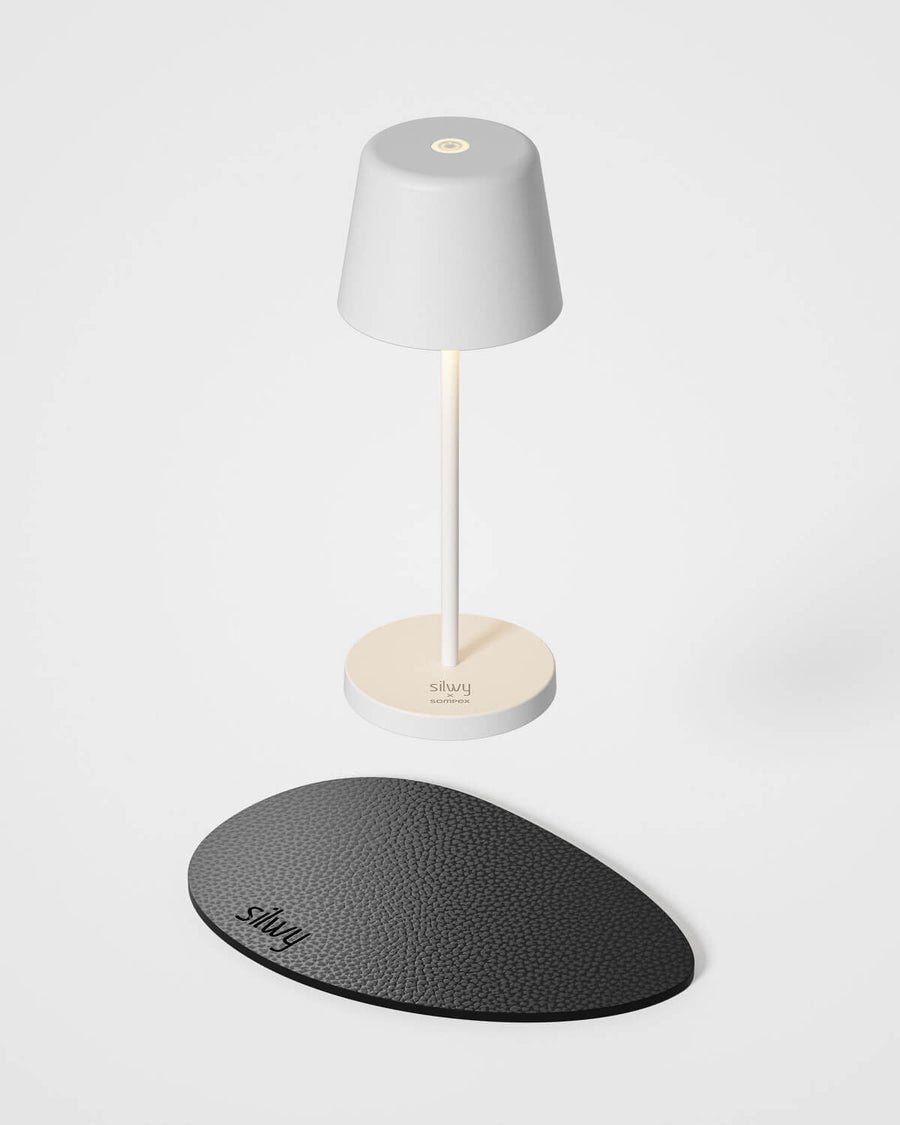 Lampe blanche de face et plateau de charge noir ovale texturé, fond blanc.