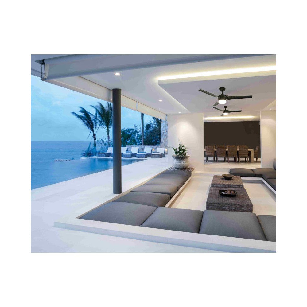 Ventilateur de plafond noir avec lumière allumée installé sous une terrasse face à la mer.