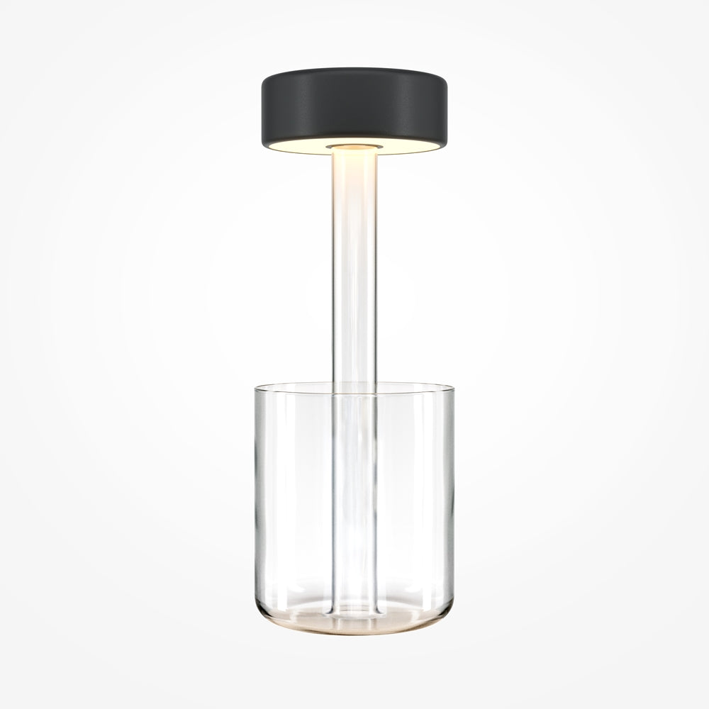 Lampe de table cylindrique, diffuseur noir, tige et socle en verre transparent, fond blanc.