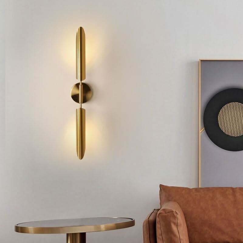 Luminaire mural allumé près d'une table basse en laiton et d'un canapé en cuir.
